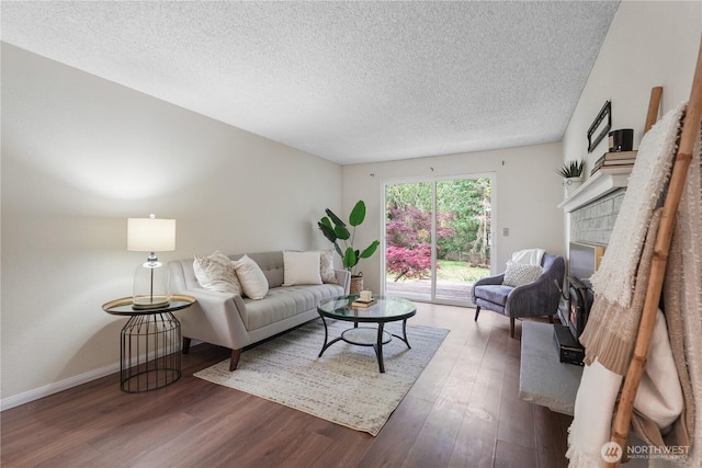 living area featuring wood finished floors, a textured ceiling, a glass covered fireplace, and baseboards