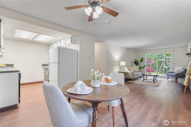 dining area with a textured ceiling, light wood-type flooring, and a ceiling fan