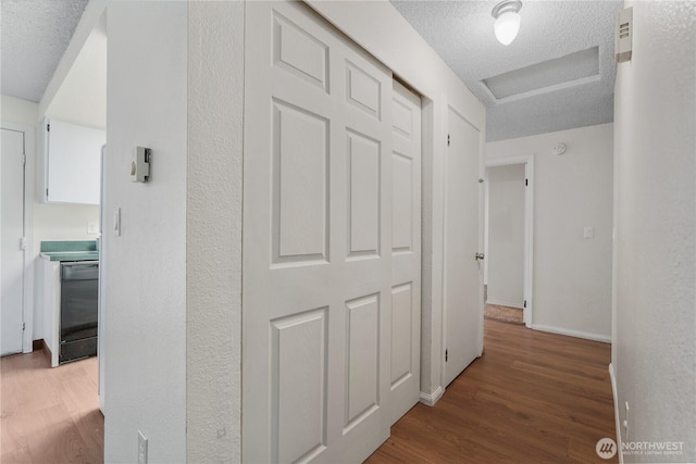 hallway featuring a textured ceiling, wood finished floors, and baseboards