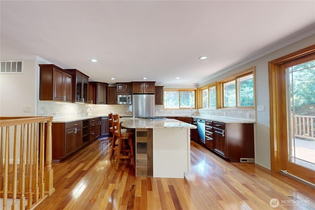 2022 Scarpelli Dr, Walla Walla, WA 99362 - kitchen featuring appliances with stainless steel finishes, light wood-type flooring, glass insert cabinets, tasteful backsplash, and crown molding