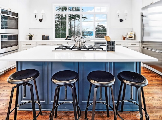kitchen featuring white cabinets, appliances with stainless steel finishes, a kitchen island, and wood finished floors