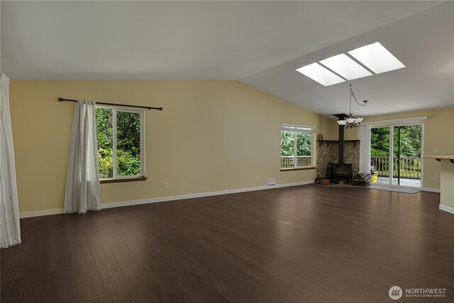 unfurnished living room featuring a skylight, vaulted ceiling, a wood stove, dark wood-style floors, and baseboards