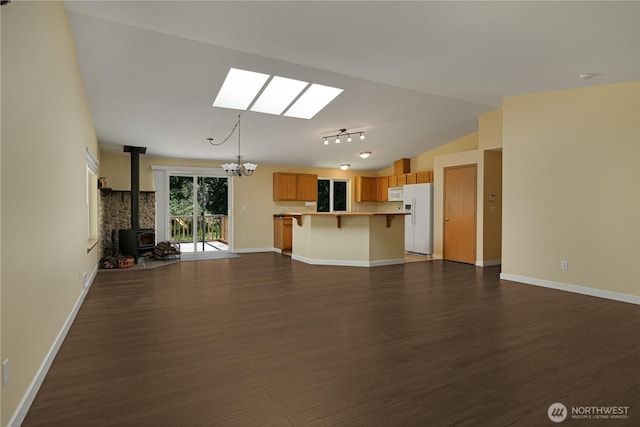 unfurnished living room featuring a skylight, a wood stove, dark wood-style flooring, vaulted ceiling, and baseboards