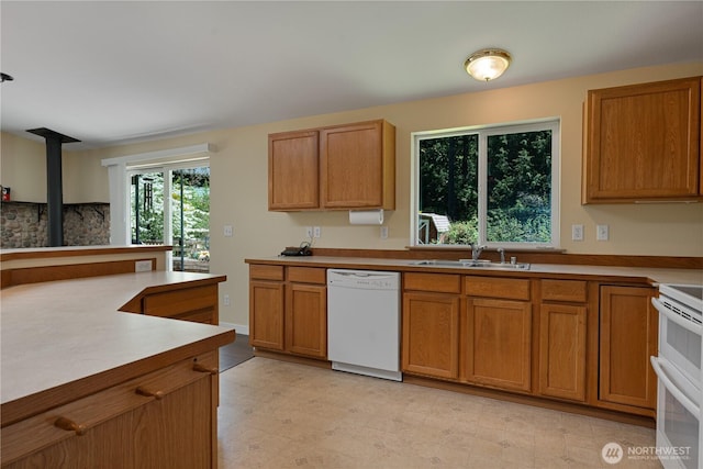 kitchen featuring white appliances, a sink, brown cabinetry, and light countertops