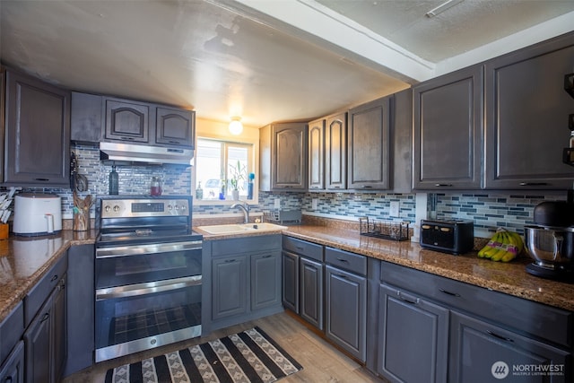 kitchen featuring double oven range, under cabinet range hood, a sink, and backsplash