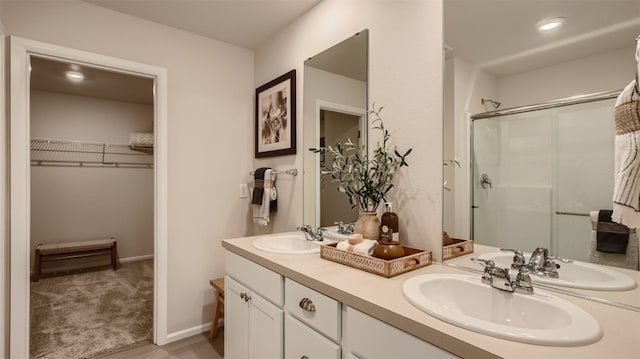 full bathroom featuring a stall shower, double vanity, a sink, and a walk in closet