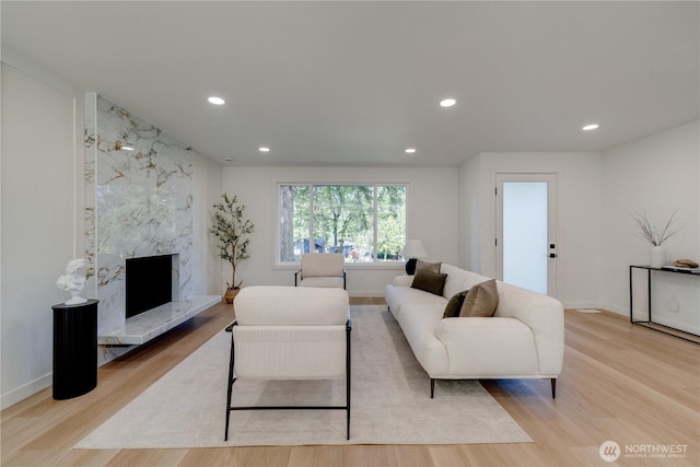living area with light wood-type flooring, recessed lighting, a premium fireplace, and baseboards