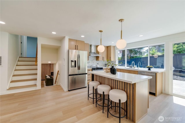 kitchen with appliances with stainless steel finishes, wall chimney exhaust hood, a breakfast bar area, light wood-type flooring, and recessed lighting