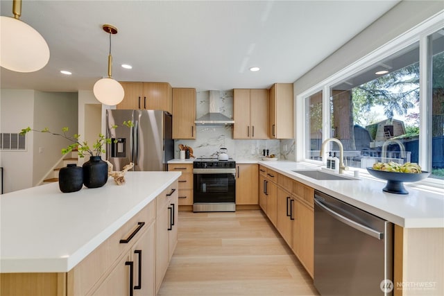 kitchen with stainless steel appliances, wall chimney exhaust hood, a sink, light brown cabinetry, and light wood finished floors