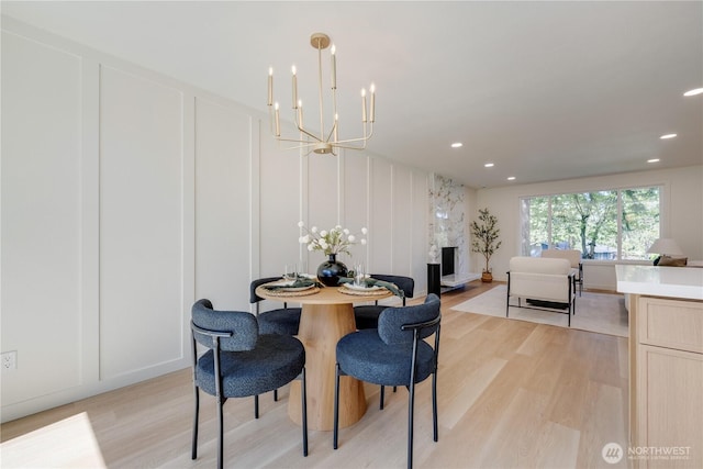 dining space with a chandelier, light wood-type flooring, a decorative wall, recessed lighting, and a premium fireplace
