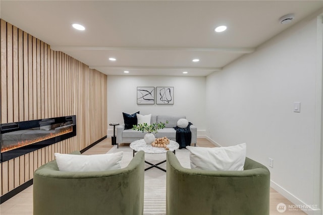 living area featuring recessed lighting, a glass covered fireplace, light wood-style floors, and baseboards
