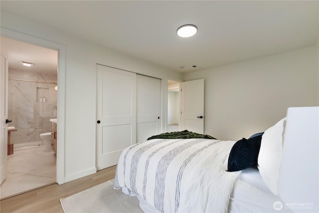 bedroom featuring a closet, ensuite bath, and light wood finished floors
