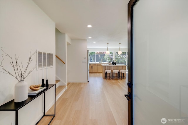 hallway featuring light wood finished floors, stairs, recessed lighting, and baseboards