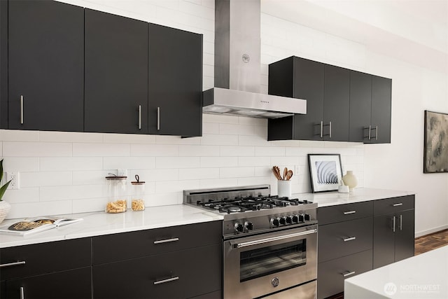 kitchen with wall chimney range hood, stainless steel stove, and dark cabinetry