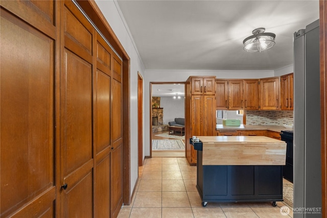 kitchen with light tile patterned flooring, brown cabinets, freestanding refrigerator, and butcher block countertops