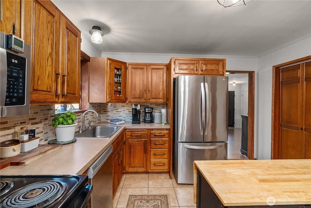 kitchen featuring stainless steel appliances, a sink, brown cabinets, tasteful backsplash, and light tile patterned floors