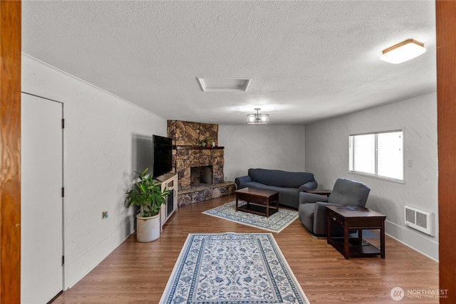 living area with a textured ceiling, wood finished floors, a stone fireplace, and attic access
