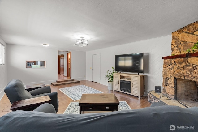 living room with a fireplace, wood finished floors, a textured ceiling, baseboards, and a chandelier