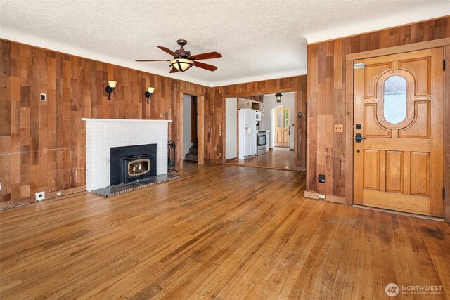25443 Pioneer Way NW, Poulsbo, WA 98370 - unfurnished living room with wooden walls, a ceiling fan, wood-type flooring, and a textured ceiling