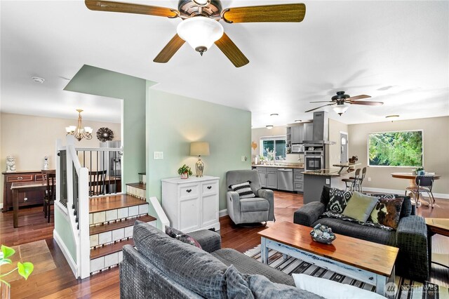 living area with a ceiling fan, a chandelier, wood finished floors, and stairs