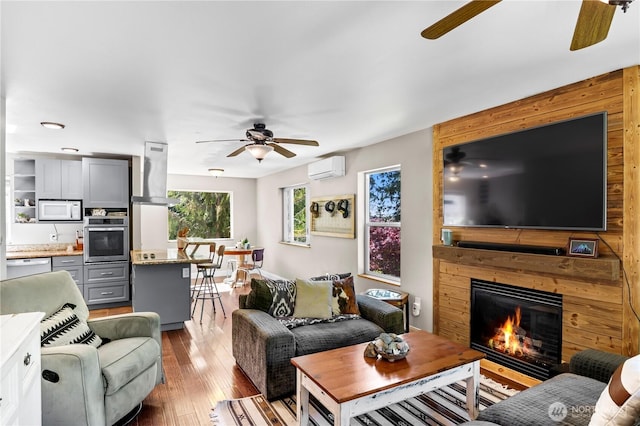 living room with ceiling fan, an AC wall unit, hardwood / wood-style flooring, and a large fireplace
