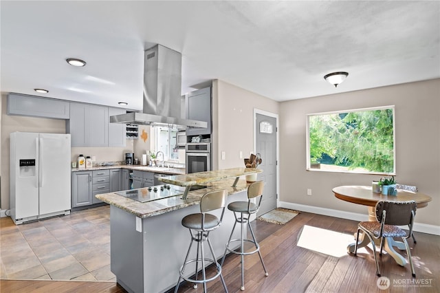 kitchen with white fridge with ice dispenser, gray cabinets, island exhaust hood, black electric cooktop, and stainless steel oven