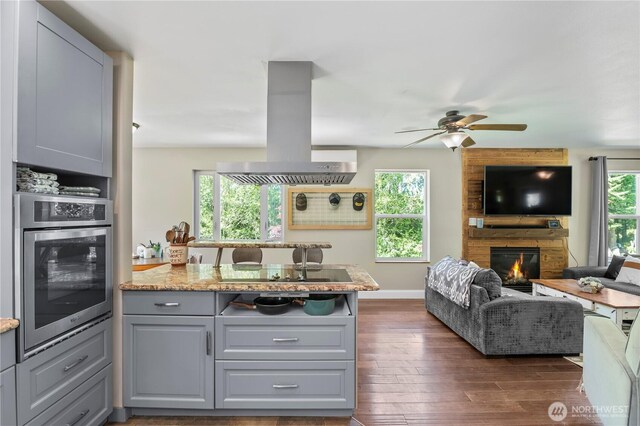 kitchen with stainless steel oven, island range hood, black electric stovetop, open floor plan, and a large fireplace