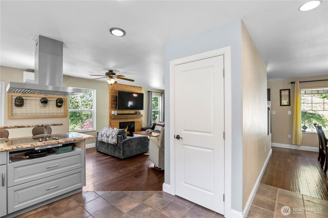 kitchen featuring a fireplace, a ceiling fan, baseboards, open floor plan, and stovetop