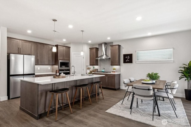 kitchen featuring stainless steel appliances, wall chimney range hood, a kitchen island with sink, a breakfast bar area, and decorative backsplash