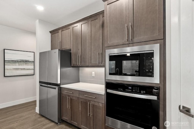 kitchen featuring tasteful backsplash, light wood finished floors, light countertops, baseboards, and appliances with stainless steel finishes