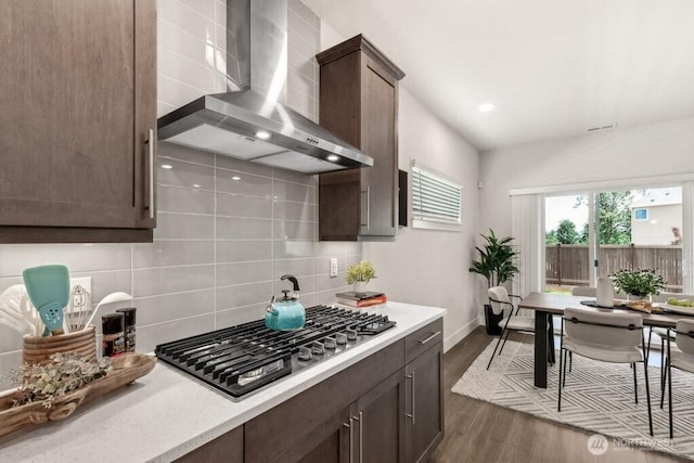 kitchen with stainless steel gas cooktop, wall chimney exhaust hood, dark wood-style flooring, decorative backsplash, and baseboards