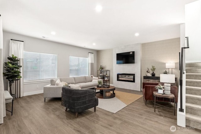 living room with a wealth of natural light, stairway, a fireplace, and wood finished floors