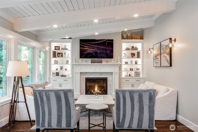 living area with a fireplace, beam ceiling, built in features, dark wood-type flooring, and baseboards