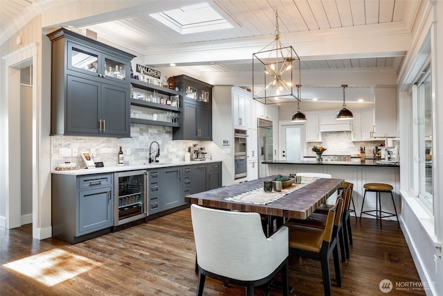 dining space featuring wine cooler, dark wood-style floors, wet bar, beam ceiling, and wooden ceiling