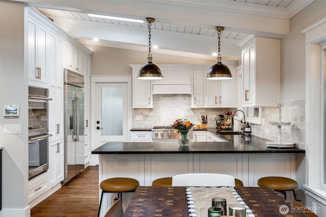kitchen featuring a sink, appliances with stainless steel finishes, a peninsula, decorative backsplash, and dark countertops