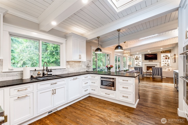kitchen featuring a sink, a lit fireplace, open floor plan, dark countertops, and beam ceiling