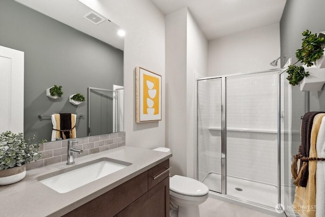 full bathroom featuring toilet, vanity, visible vents, decorative backsplash, and a shower stall