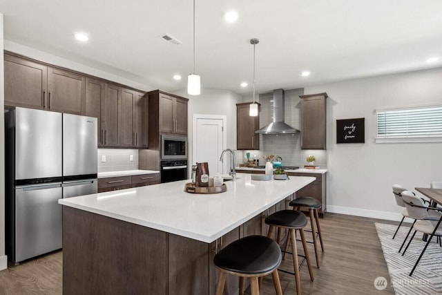 kitchen with backsplash, stainless steel appliances, wall chimney exhaust hood, and dark brown cabinetry