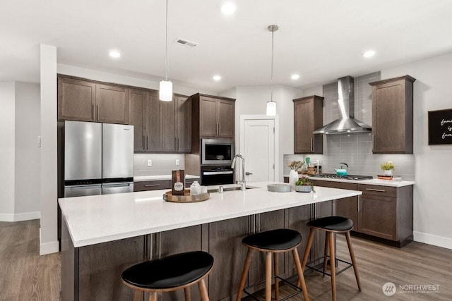 kitchen featuring dark brown cabinets, stainless steel appliances, visible vents, baseboards, and wall chimney range hood