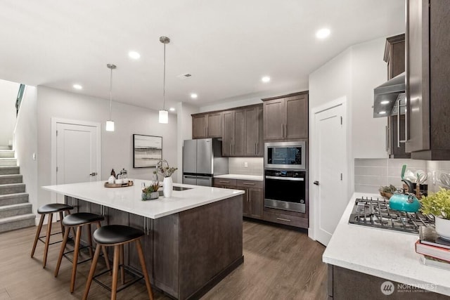 kitchen with a sink, stainless steel appliances, dark wood finished floors, light countertops, and dark brown cabinets