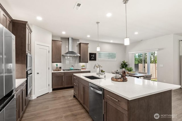 kitchen with wall chimney exhaust hood, stainless steel appliances, wood finished floors, and a sink