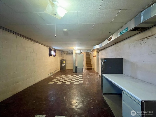 finished basement featuring dark flooring, electric water heater, stairway, heating unit, and concrete block wall