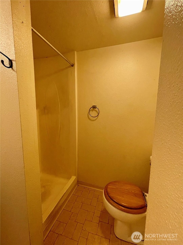 full bathroom featuring a stall shower, toilet, and brick patterned floors