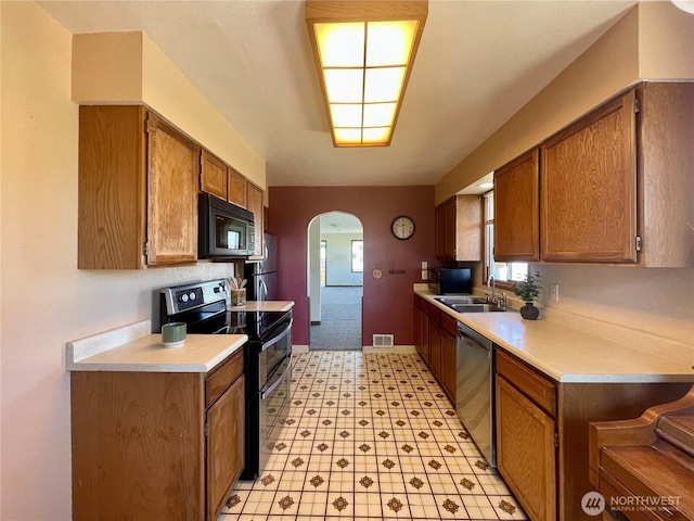 kitchen with stainless steel appliances, arched walkways, light countertops, a sink, and brown cabinets