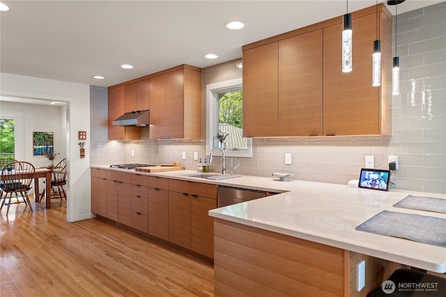 kitchen with light countertops, light wood-type flooring, a sink, and backsplash