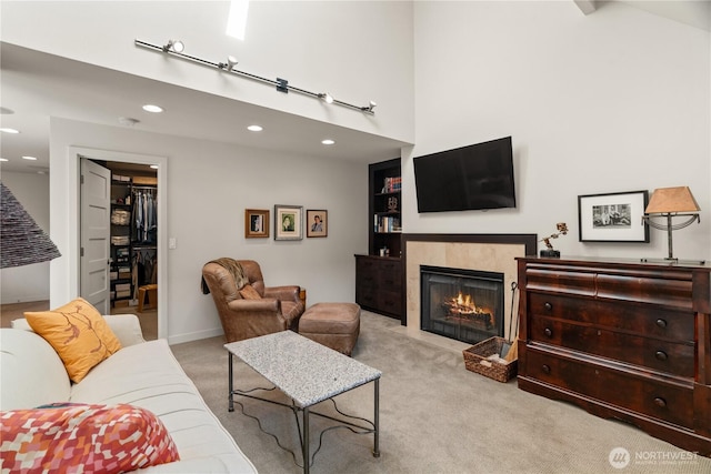 carpeted living room featuring a warm lit fireplace, baseboards, a high ceiling, and recessed lighting