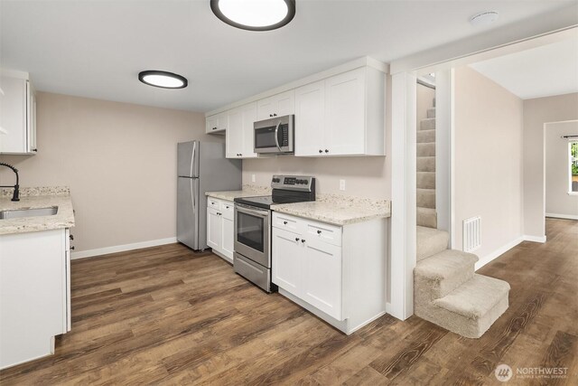 kitchen with appliances with stainless steel finishes, a sink, dark wood-style floors, baseboards, and white cabinetry
