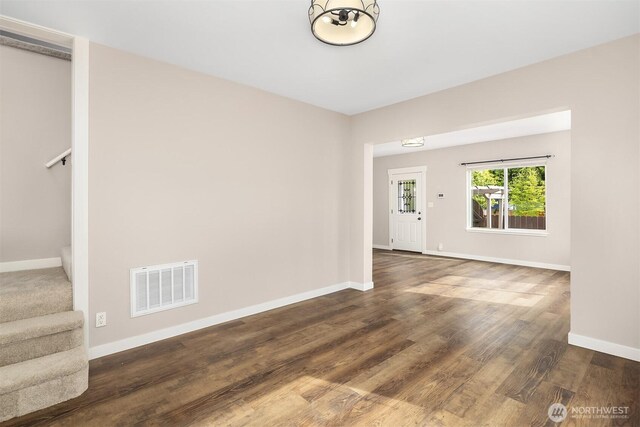 empty room featuring baseboards, stairs, and dark wood-style floors