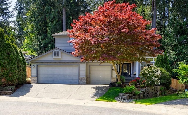 view of property hidden behind natural elements featuring concrete driveway, an attached garage, stone siding, and fence
