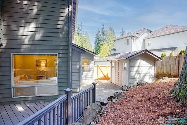 view of side of property featuring fence, a wooden deck, and an outbuilding